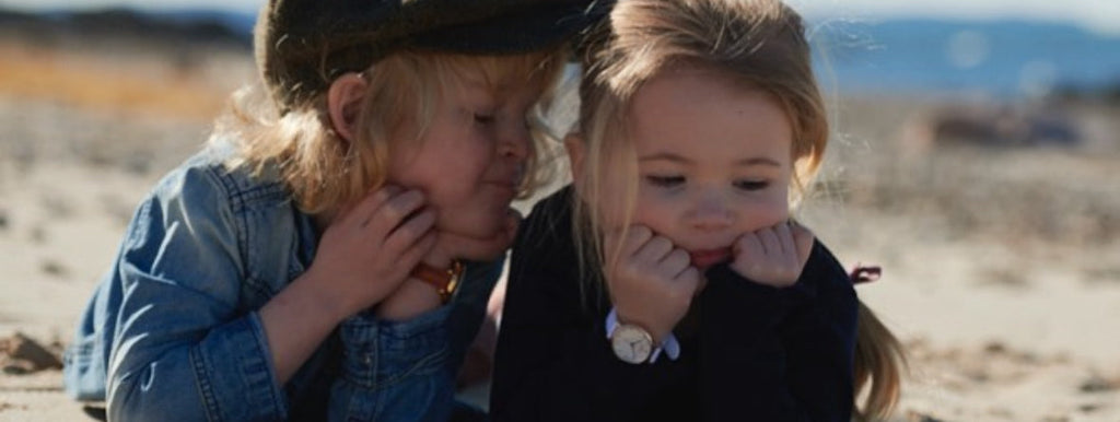 Analog klocka för barn, här en liten pojke med klockor. Pojken viskar något till den lilla flickan på stranden - Torekovs