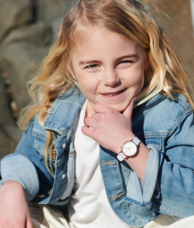 Söt flicka på stranden som bär en roséfärgad Torekovs-barnklocka med vitt tygband.